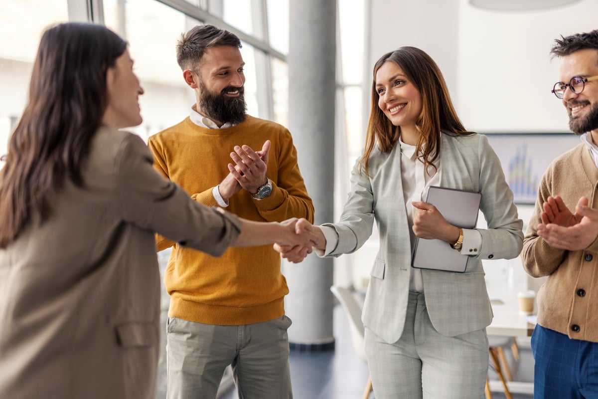 Two successful female executives shaking hands for partnership with team celebrating success
