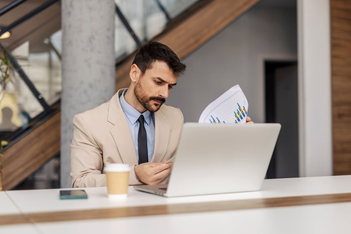 Portrait of focused corporate worker sitting at office with documents in hands and analyzing data