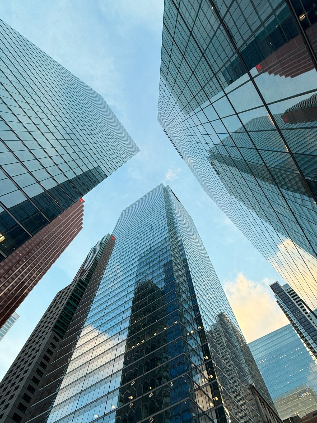 Low angle view of modern glass skyscrapers reflecting the sky and surrounding city buildings